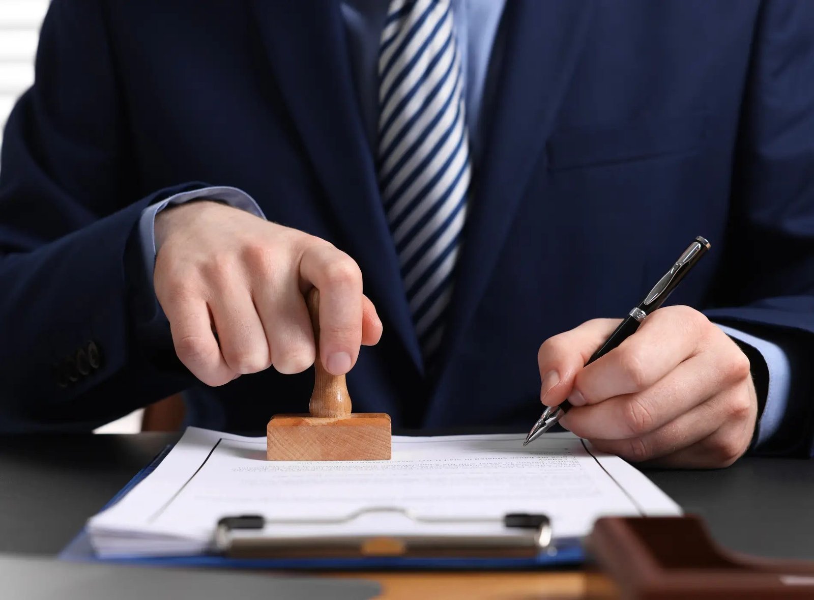A CPA stamping and signing an attestation report at a desk, close on the hands and the document
